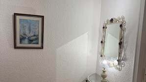 A bathroom with a white textured wall, a framed painting, a vanity with a mirror, and a light fixture above the mirror. - Apparently 2 rooms (Vaulx-en-Velin)