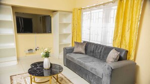 Una sala de estar con un sofá gris, una mesita redonda con un florero y cortinas amarillas.