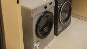 Un lavadero con dos lavadoras, un estante con botellas de detergente y una puerta.