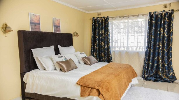 Un dormitorio con cama, almohadas, colcha, cortinas y decoración en la pared.