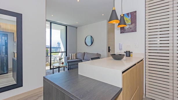 Una cocina moderna con una isla central, un área de comedor con sofá y un ventanal que ofrece vistas a la ciudad.