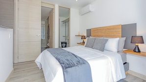 Un dormitorio moderno con una cama grande, cabecera de madera, mesita de noche con lámpara y un cesto de ropa.