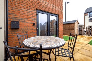 A patio with a round table and chairs, a brick wall, and a glass door.