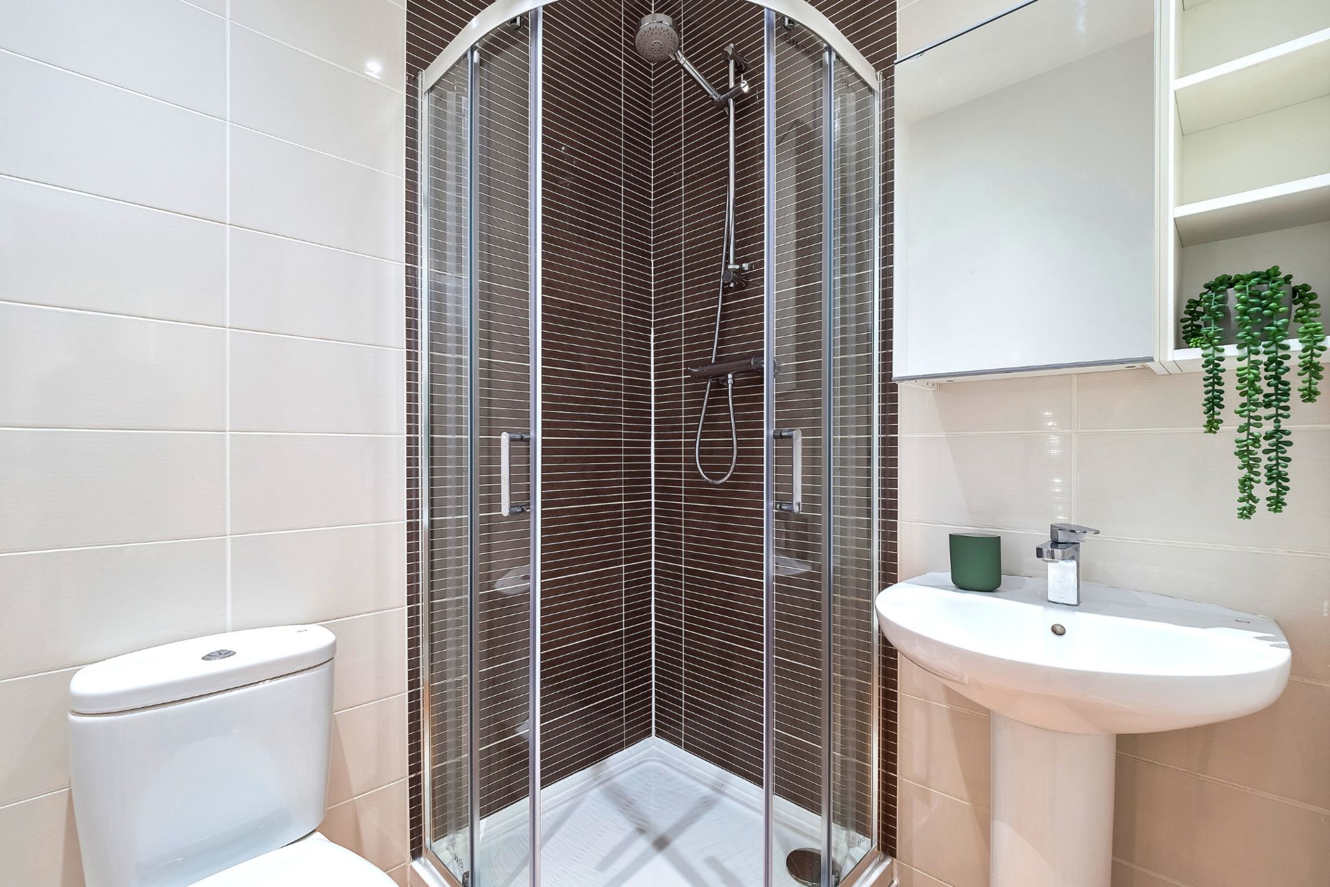 Ein modernes Badezimmer mit einer gläsernen Duschkabine, einer weißen Toilette und einem Waschbecken mit grünem Seifenspender.