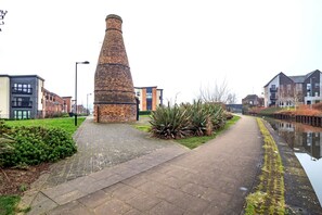 A brick chimney, a paved walkway, and modern buildings along a canal.