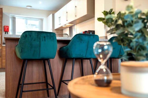A modern kitchen with two teal bar stools, a wooden countertop, and a potted plant on a round table.