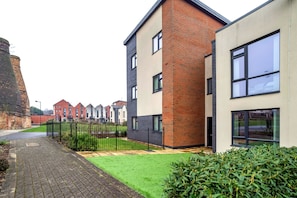 A modern residential building with a brick facade, large windows, and a well-maintained lawn.