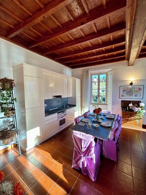 A kitchen with white cabinets, a granite countertop, and a dining area with a purple tablecloth. - Elegant Apartment inside Villa Fontana (Tremezzo)