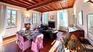 Un salón amplio con chimenea, sofá de cuero, mesa de comedor preparada para cuatro personas y grandes ventanales que ofrecen vistas al exterior.