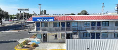 Un motel avec une enseigne « Bienvenue », plusieurs chambres, un parking délimité par une clôture et un magasin Walmart en arrière-plan.