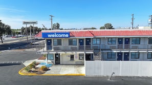 A motel with a 'Welcome' sign, multiple rooms, a fenced parking area, and a Walmart store in the background.