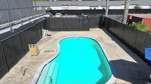 A swimming pool with a metal ladder, surrounded by a black fence, and a parking area with cars.