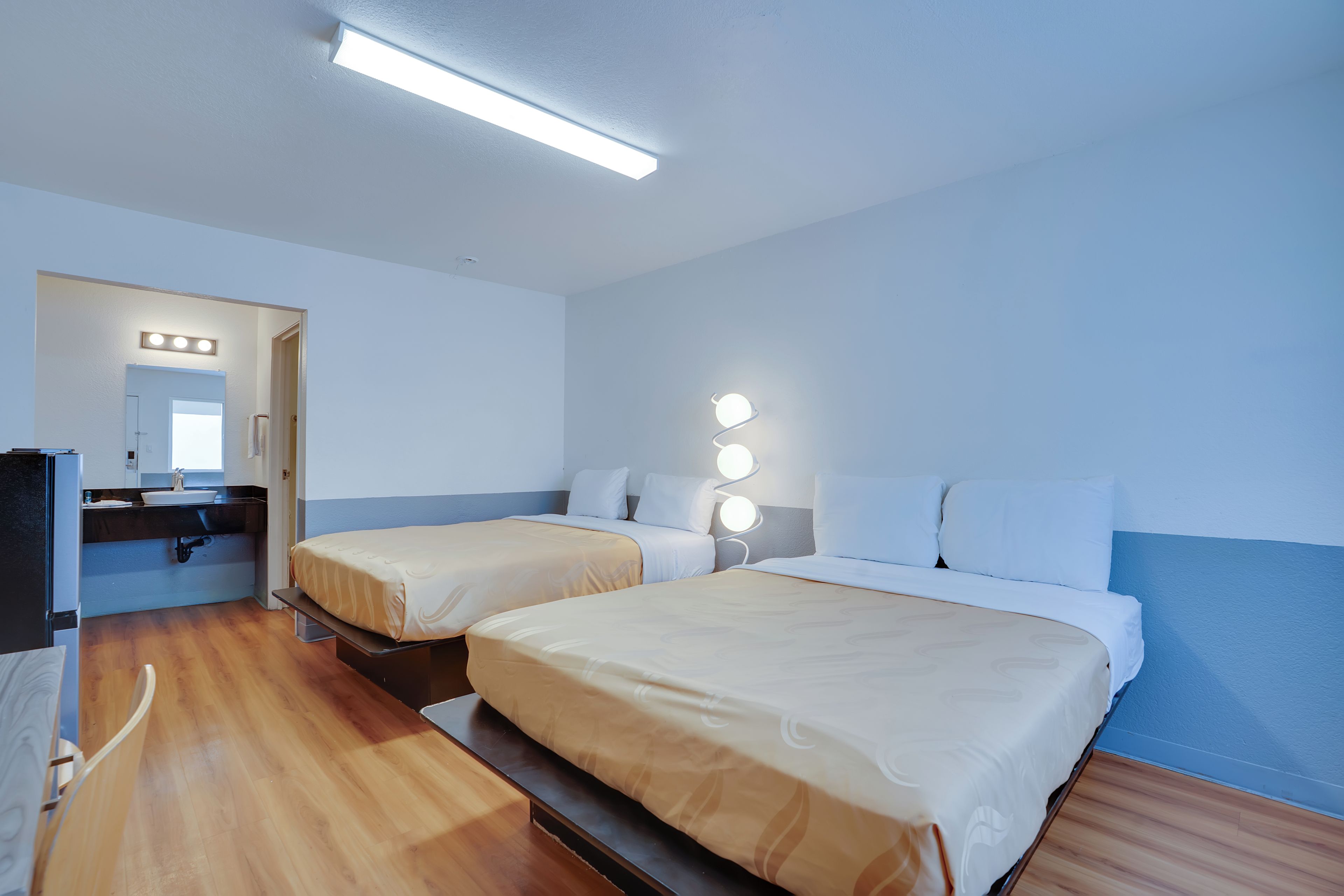 Une chambre d’hôtel avec deux lits, un bureau avec un ordinateur, un miroir et un luminaire fixé au mur.