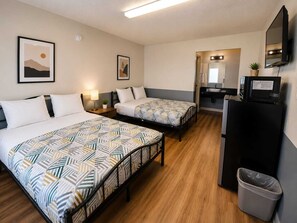 A hotel room with two beds, a desk, a mirror, a television, and a trash bin.