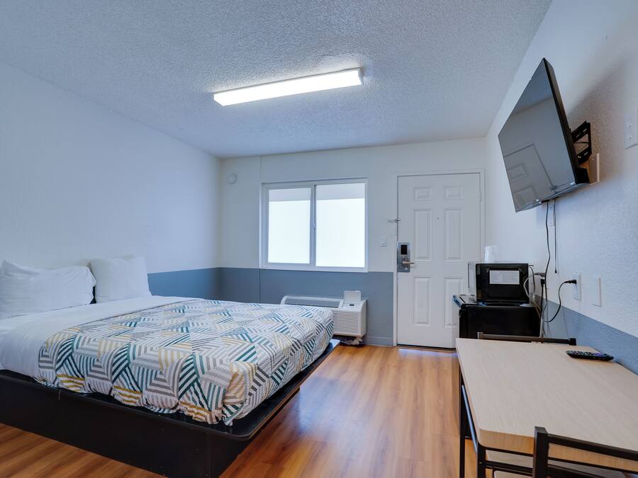 Een slaapkamer met een bed, bureau, televisie en raam.