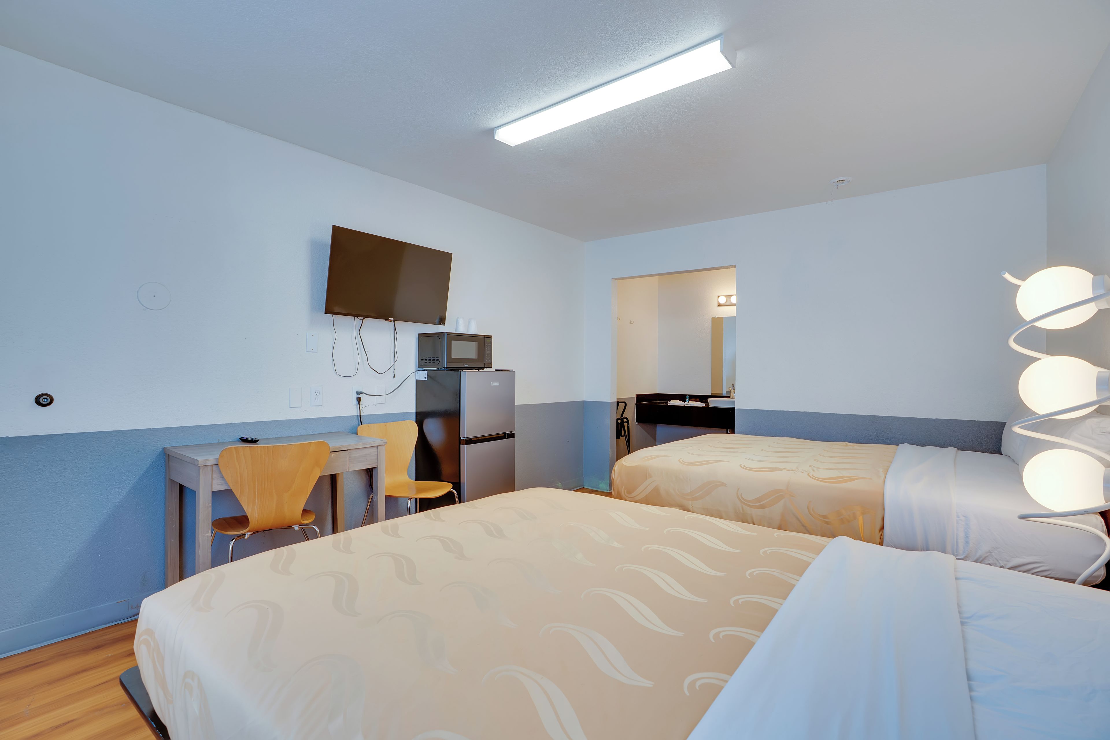 Ein Hotelzimmer mit zwei Betten, einem Schreibtisch, einem Stuhl, einem Fernseher und einem Spiegel.