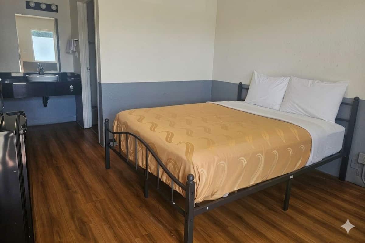 A single bed with a headboard, a bedside table, a mirror, and a sink in a room with wooden flooring.