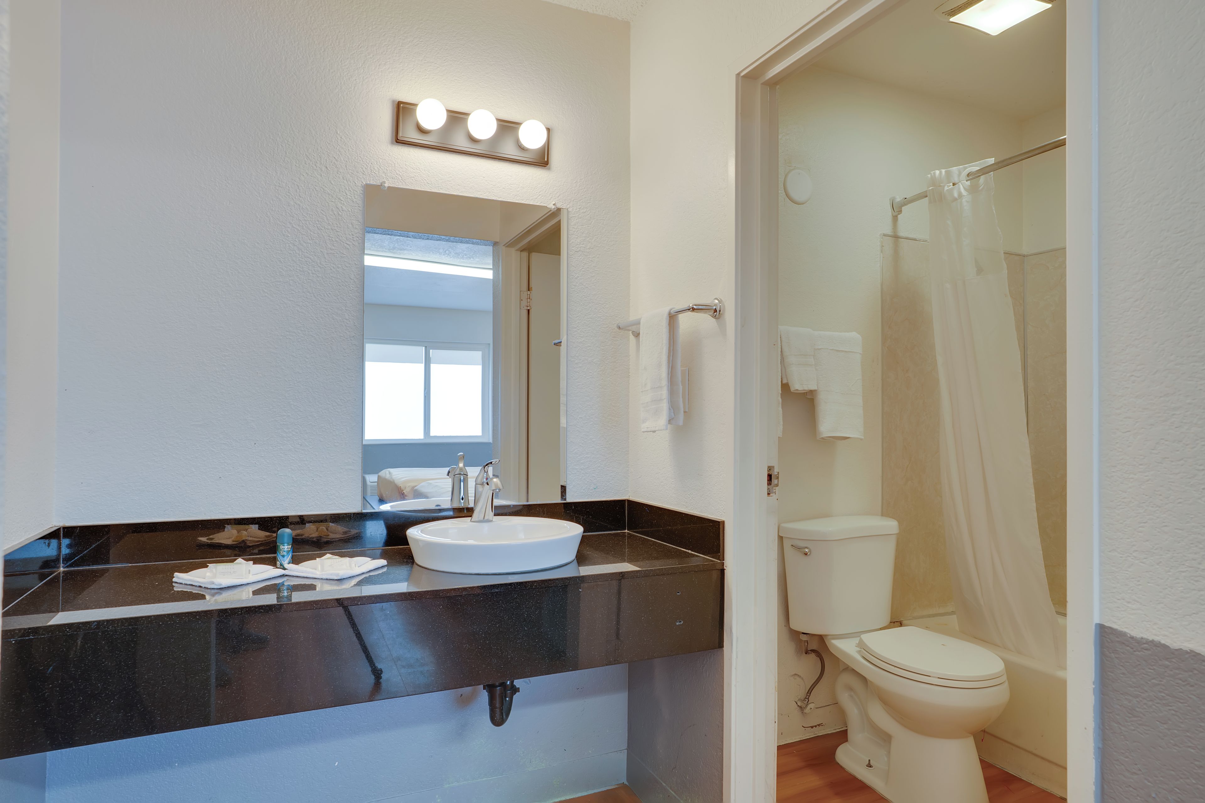 Een badkamer met een witte wastafel, een spiegel met verlichting, een douchegordijn en een toilet.