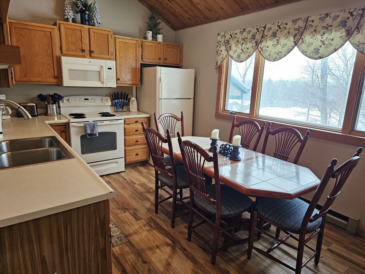 A kitchen with wooden cabinets, a microwave, stove, refrigerator, and a dining table with chairs.