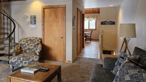 Un salon chaleureux avec un fauteuil à motifs, un canapé, une table basse en bois et un escalier menant à l’étage supérieur.