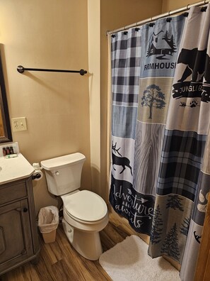 Et badeværelse med toilet, vask og bruseforhæng med et landbrugs- og junglemotiv.