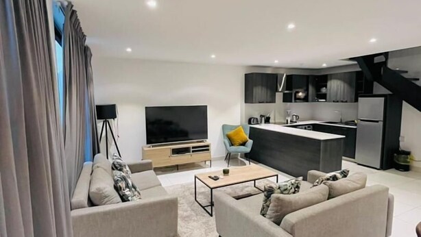 A modern living room with a sofa, coffee table, and TV. - Peravi Suites at The Lennox (Accra)