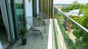A balcony with two wicker chairs, a potted plant, and a view of a cityscape. - Peravi Suites at The Lennox (Accra)