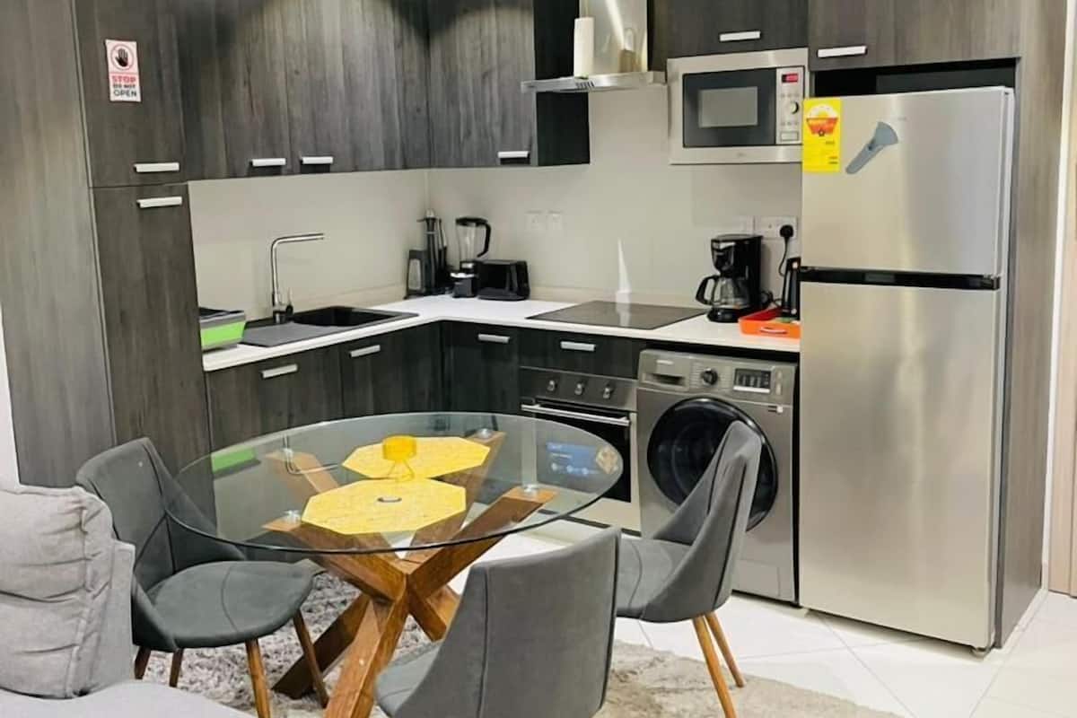 Una cocina moderna con una isla central, electrodomésticos integrados y un comedor con una mesa de vidrio.