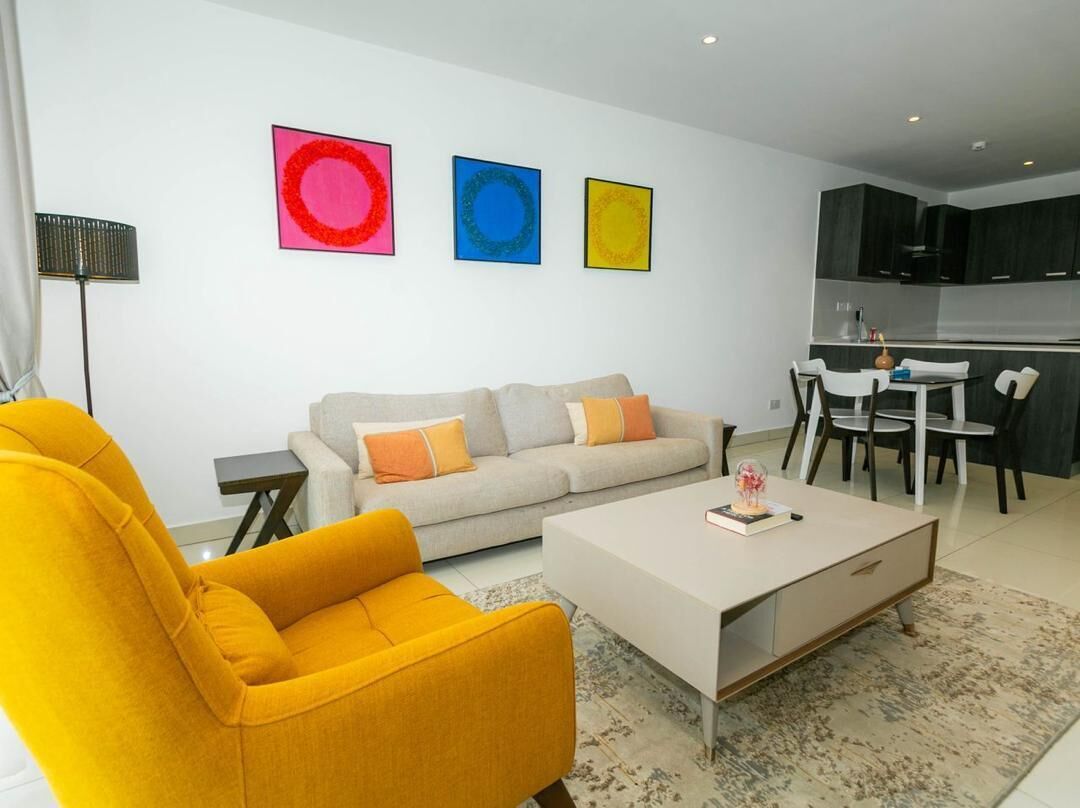 A modern living room with a sofa, a yellow armchair, and a coffee table. There are three framed artworks on the wall.