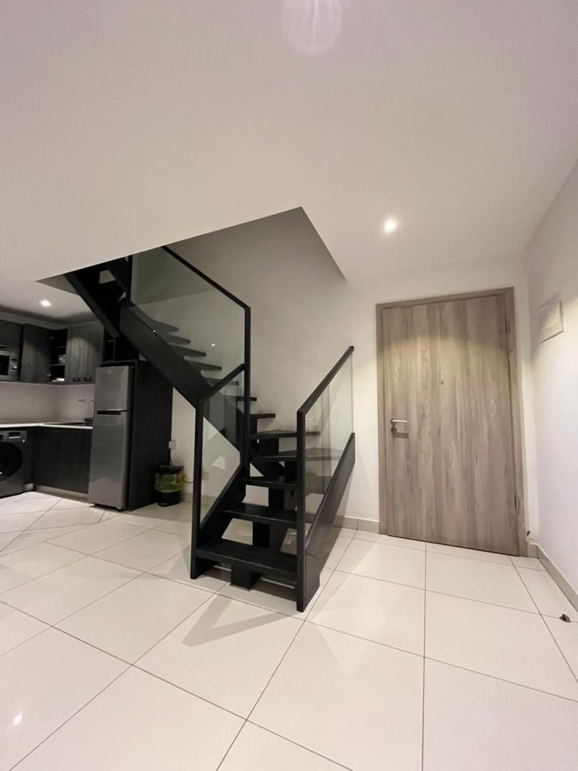 A modern kitchen with a built-in oven, a stainless steel refrigerator, and a black staircase with glass railings.