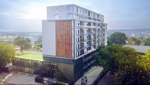 A modern multi-story hotel with a glass facade, a rooftop terrace, and a view of the surrounding landscape. - Peravi Suites at The Lennox (Accra)