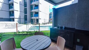 A modern outdoor seating area with a pool, a bar, and a view of high-rise buildings. - Flats Garden no Nomar Carneiros Ecoloving (Tamandaré)