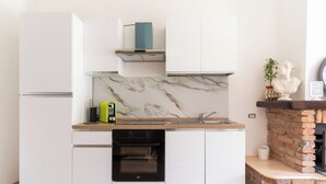 Eine kompakte Küche mit weißen Schränken, einer Marmor-Spritzschutzwand, einem eingebauten Backofen und einem Kamin aus Backsteinen.