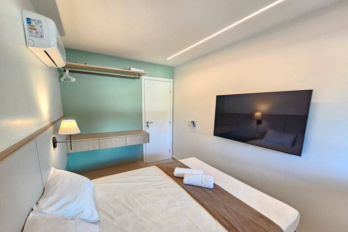Habitación de hotel con cama, televisor montado, aire acondicionado de pared y toalla sobre la cama.
