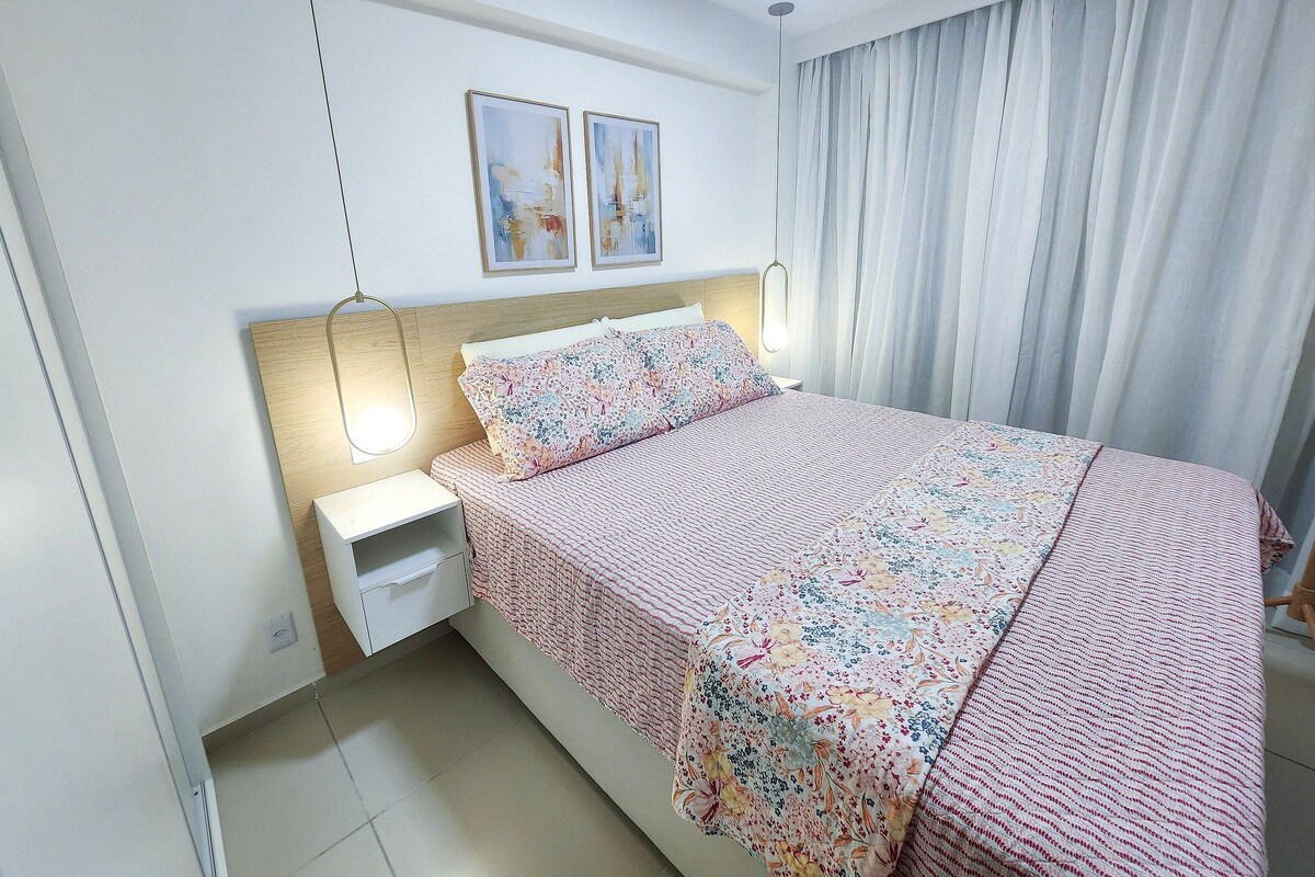 A bedroom with a bed, nightstand, wall art, and curtains.