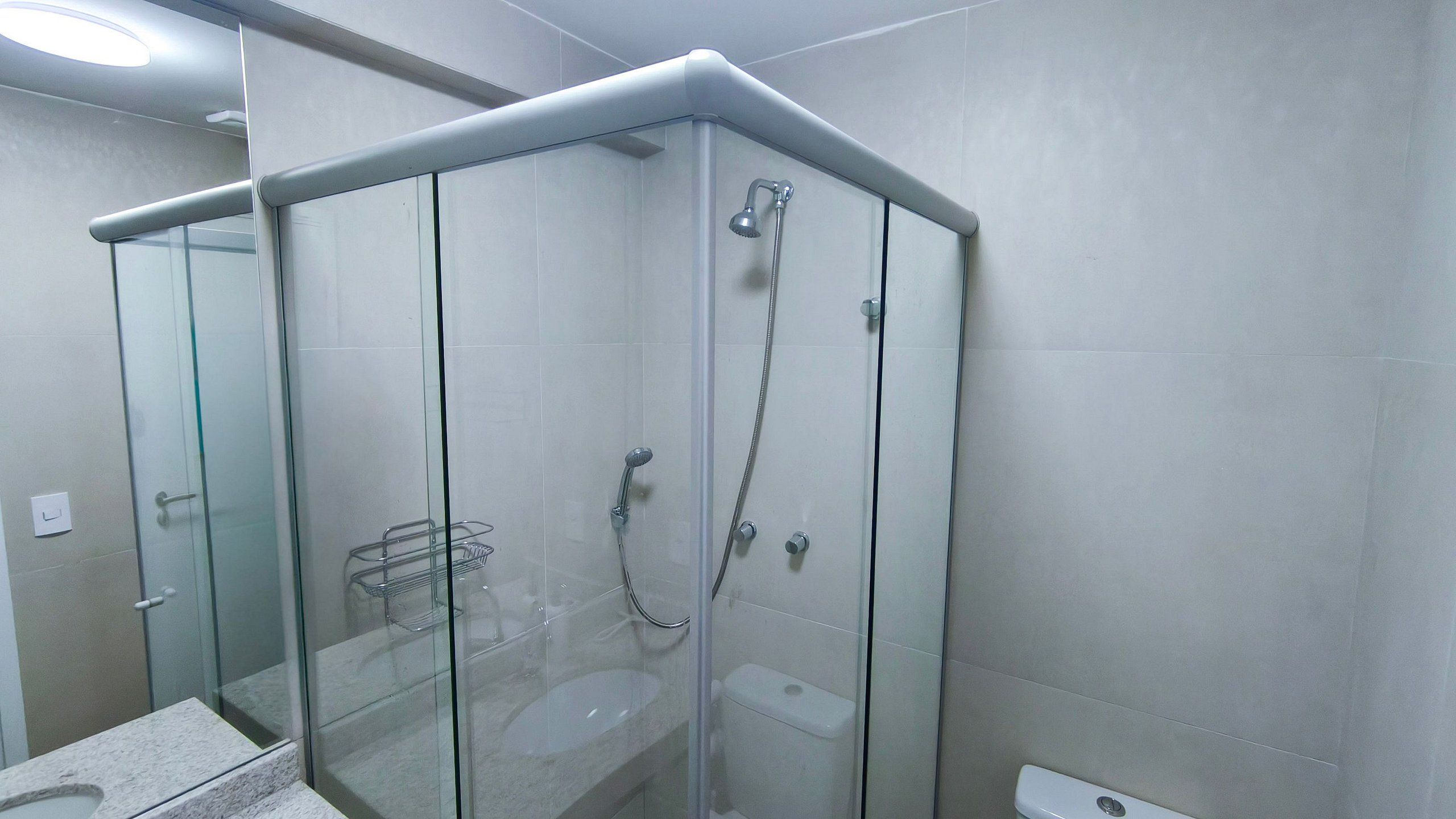 A glass-enclosed shower with a handheld showerhead and a wall-mounted faucet.