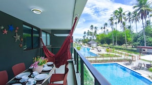 A balcony with a pool view, red chairs, dining table, and starfish decorations. - Galapagos Beach Residence - Praia dos Carneiros (Tamandaré)