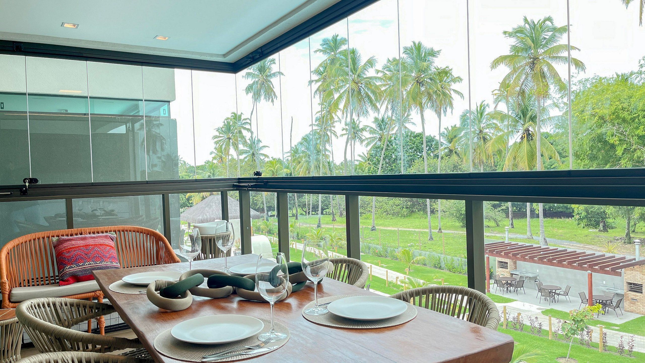 A dining area with a table set for two, overlooking a lush garden with palm trees.