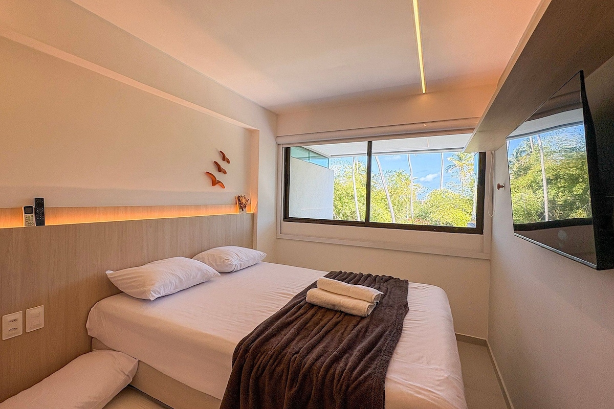 Ein modernes Schlafzimmer mit Bett, Nachttischlampen, einem Fenster mit Blick und einem an der Wand befestigten Flachbildfernseher.