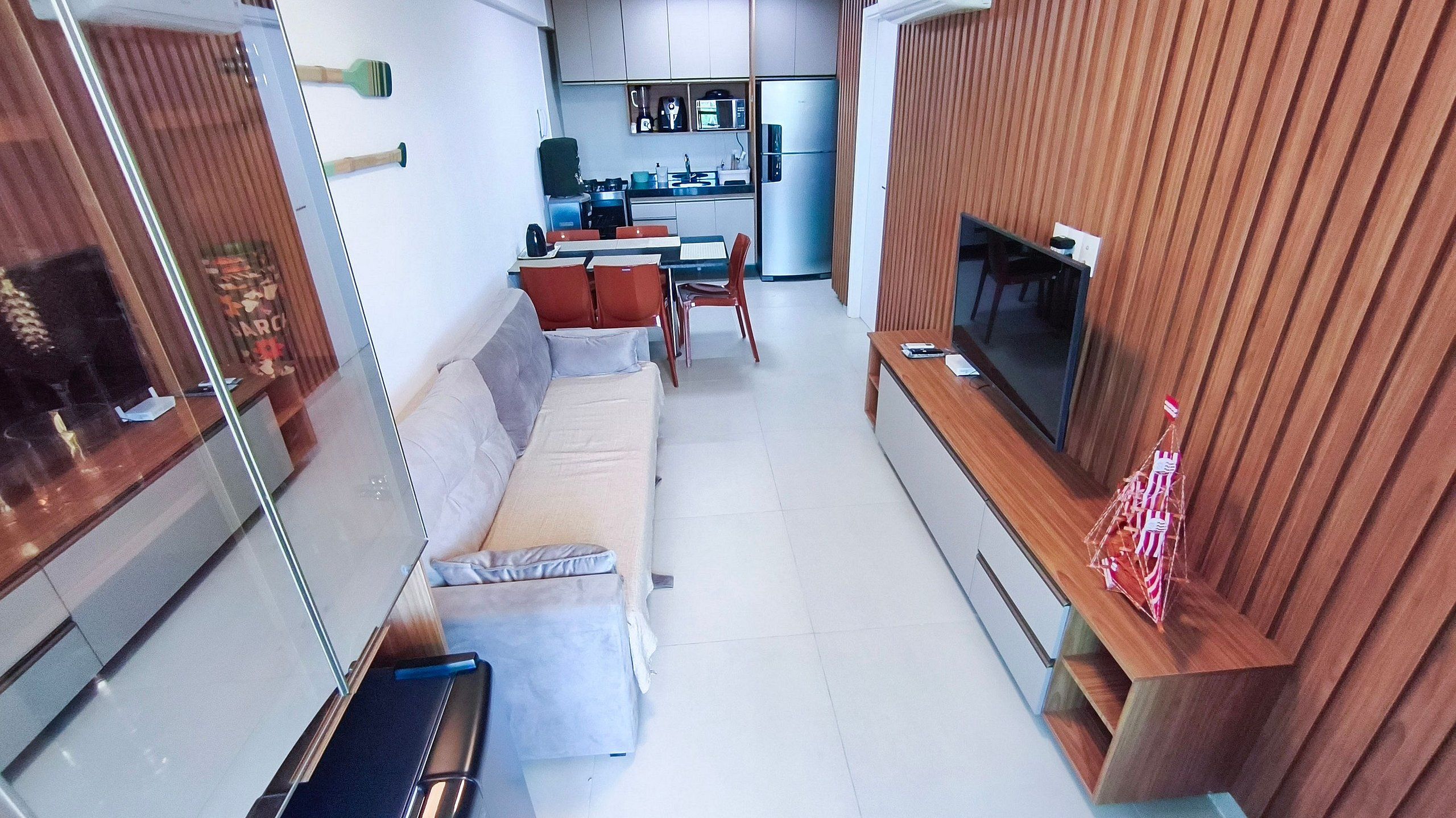 Ett kompakt bostadsutrymme med en soffa, en tv, ett köksområde och en vägg av trä.