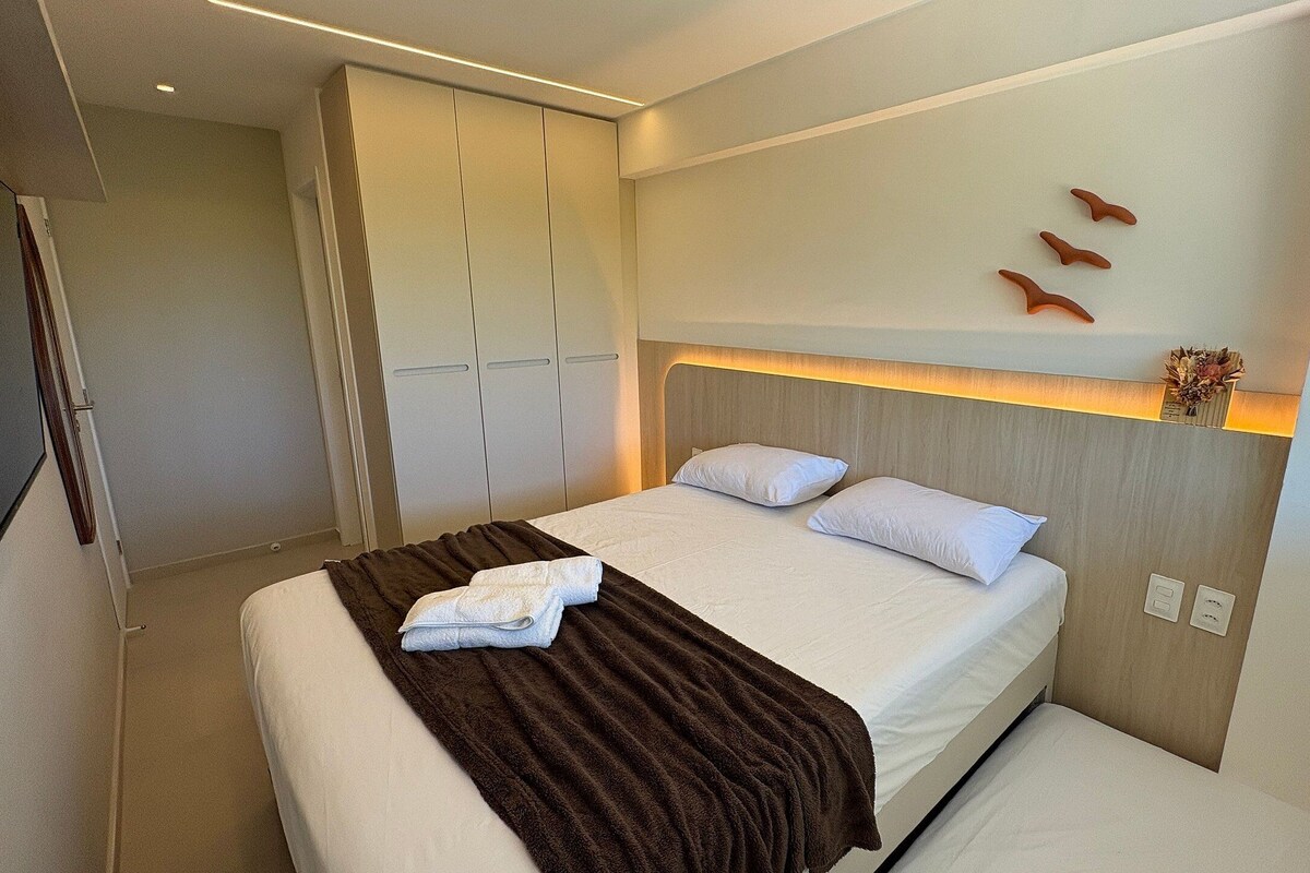 A modern hotel room with a large bed, a bedside table, and a wardrobe.