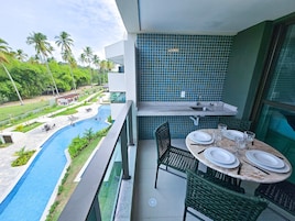 Un balcón con vista a una piscina, una mesa de comedor dispuesta con platos y vasos, y un salpicadero de azulejos.