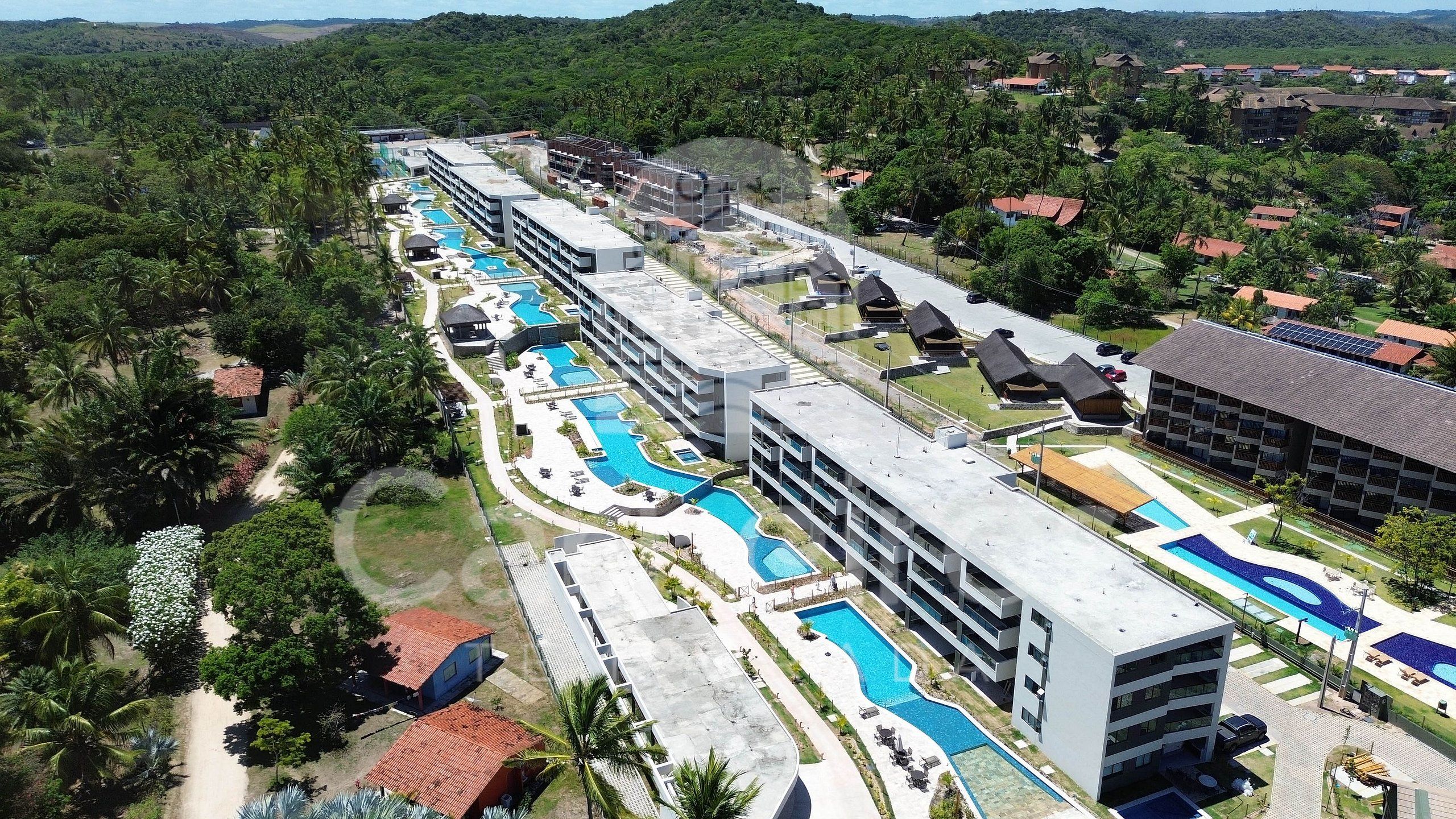 A resort with multiple swimming pools, a large building with balconies, and a surrounding landscape with trees.