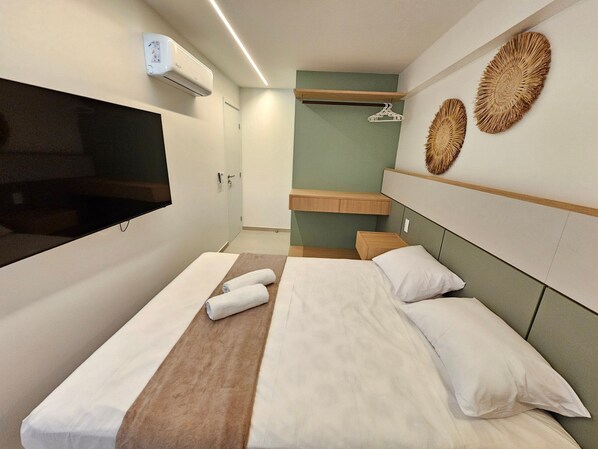 Una habitación de hotel moderna con una cama, un televisor, un aire acondicionado instalado en la pared y un estante de madera.