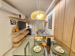 Una sala de estar moderna con un sofá, un televisor, una mesa de comedor con manteles individuales verdes y una lámpara colgante.