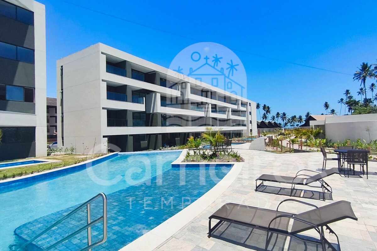 A modern hotel with a swimming pool, outdoor seating, and a clear view of the surrounding palm trees.
