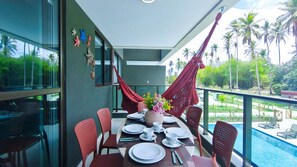A dining area with a table set for four, chairs, a pool, and a view of palm trees. - Galapagos Beach Residence - Praia dos Carneiros (Tamandaré)