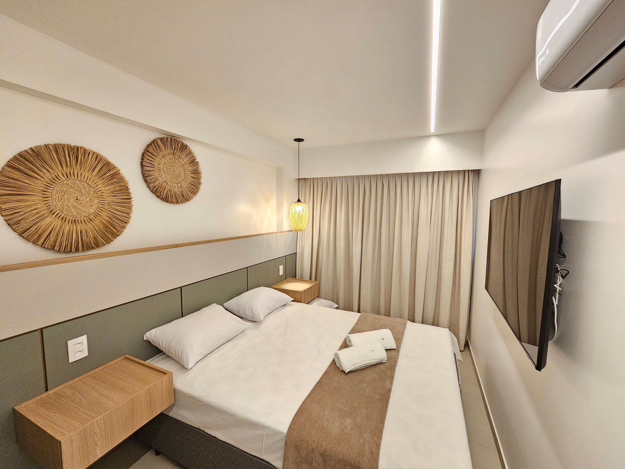 A modern hotel room with a bed, bedside tables, a wall-mounted TV, and decorative wall art.