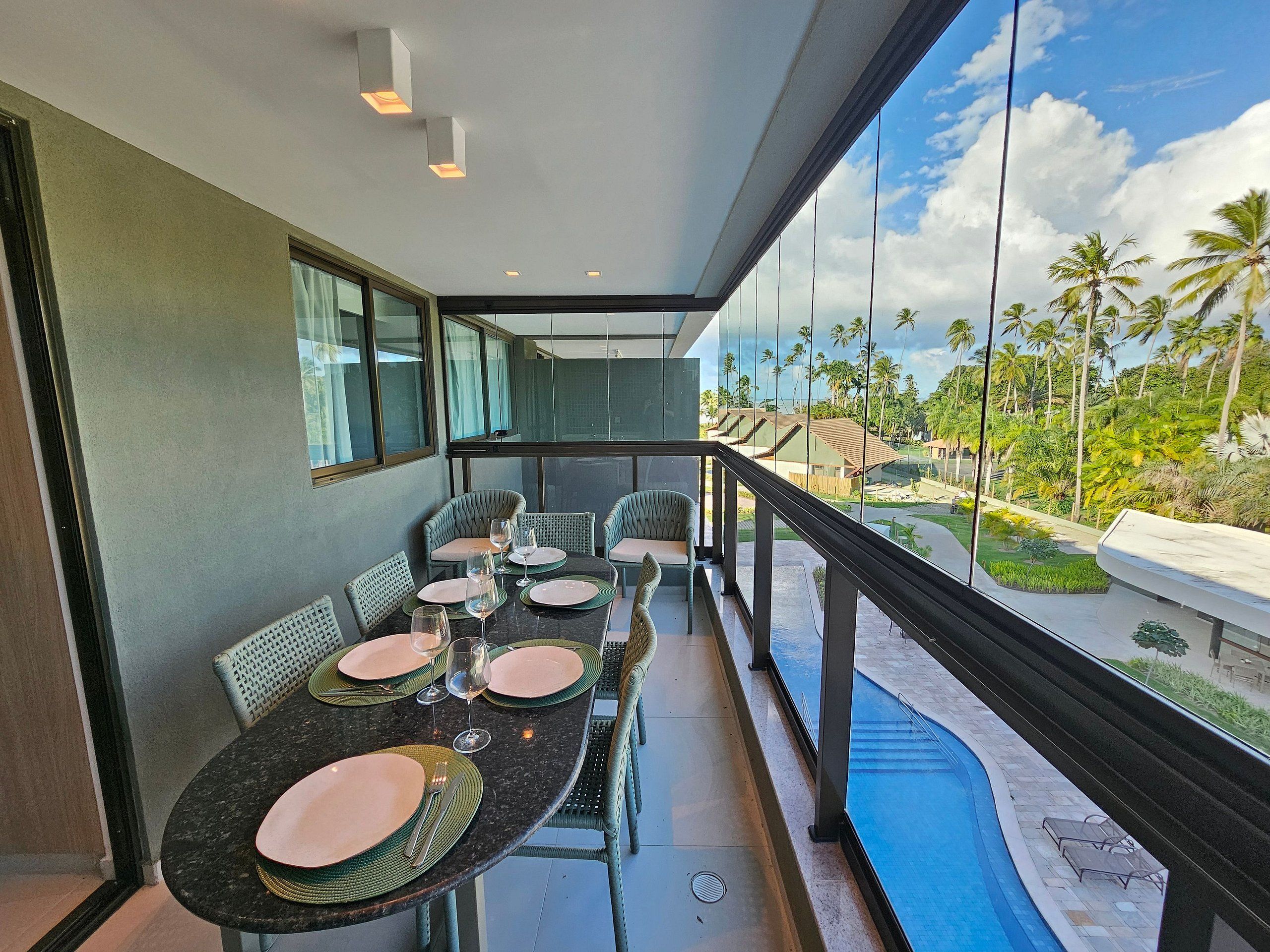 A balcony with a dining table set for four, overlooking a pool and palm trees.