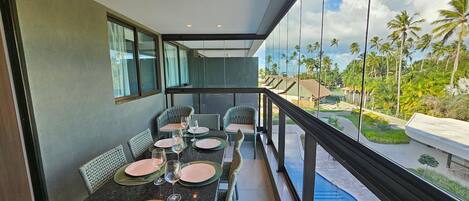 A balcony with a dining table set for four, overlooking a pool and palm trees.